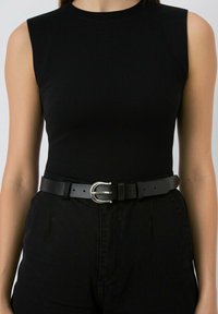 Zwarte mouwloze top met een ronde hals, gecombineerd met hoge zwarte broek en een zwart leren riem met een zilveren dubbele lusgesp.