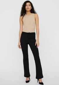 Top sans manches beige associé à un pantalon évasé noir. Le top a une texture lisse, tandis que le pantalon présente un design ajusté et un léger stretch.