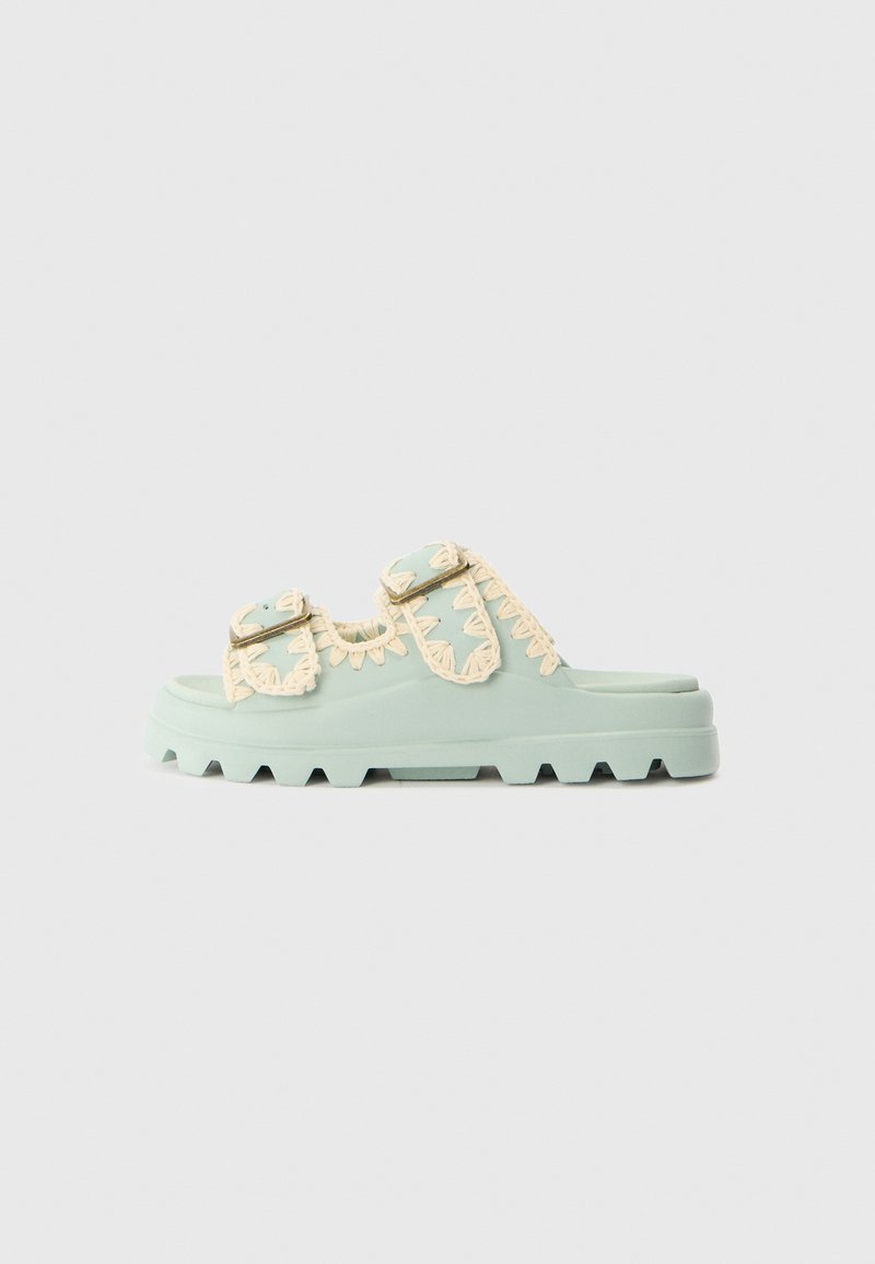 Light green platform sandals with cream decorative straps and metal buckles. Thick textured sole with a rugged pattern.