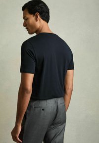 Tricou negru cu mânecă scurtă, fabricat dintr-un material moale, asortat cu pantaloni gri care au un buzunar pe spate și un design elegant.