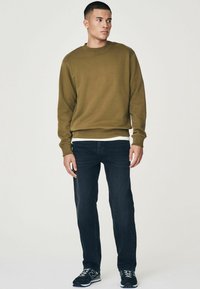 Sudadera verde oliva con cuello redondo, puños y dobladillo de canalé; combinada con jeans de mezclilla oscura y zapatillas negras. Diseño simple, sin patrones.