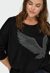 Black long-sleeve sweatshirt featuring a stylized silver rhinestone wing design on the front. Soft, relaxed fit, and round neckline.