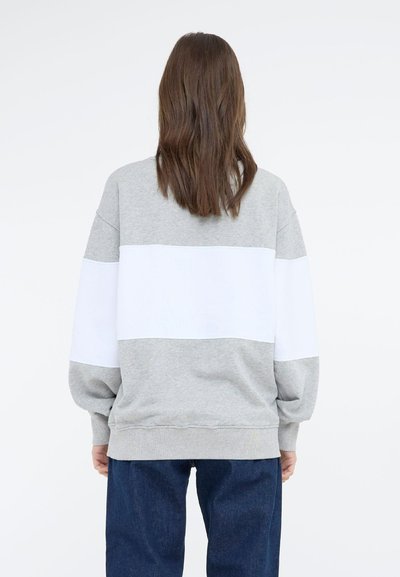 Grå hettegenser med en hvit horisontal stripe på midten, løs passform, ribbestrikkede mansjetter og myk tekstur, sammen med mørkeblå jeans.