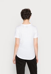 Bílé tričko s krátkým rukávem a kulatým výstřihem, z hladké bavlněné tkaniny, s mírně zakřiveným lemem na zádech. Minimalistický design, bez grafiky.