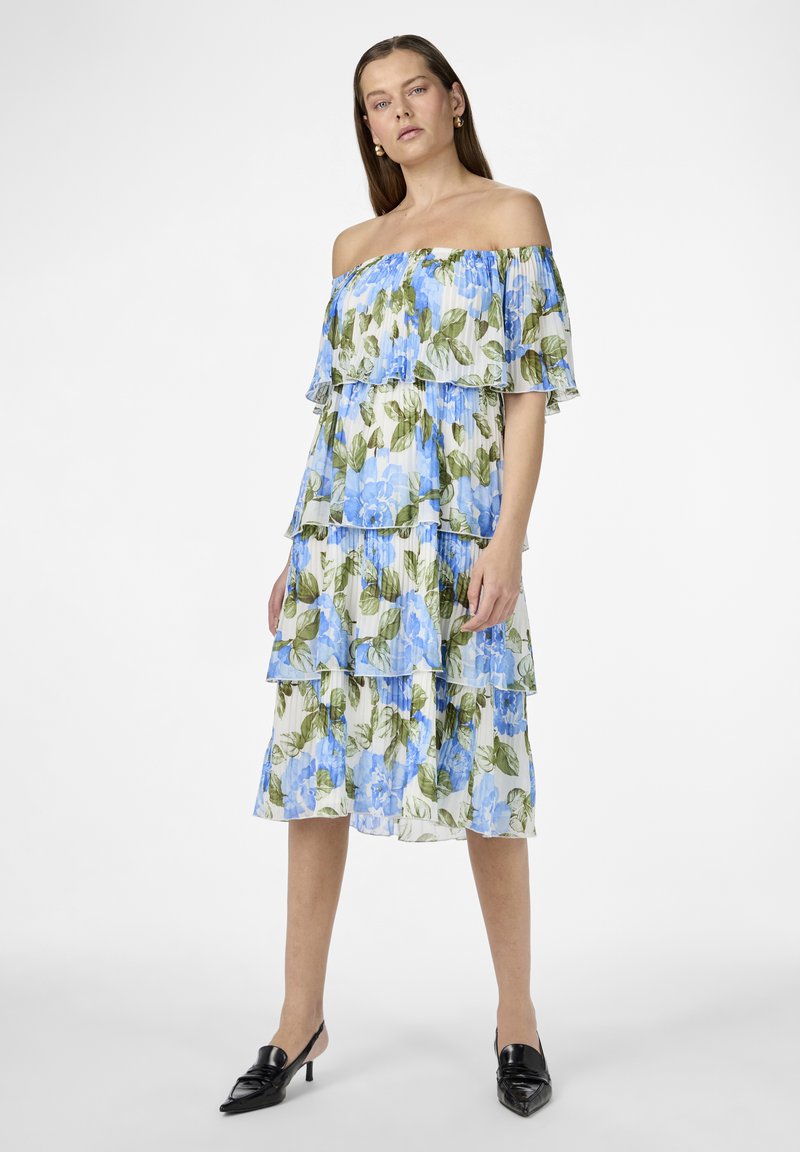 Robe décolletée avec des volants superposés, motif floral bleu sur fond blanc, en tissu léger et fluide.