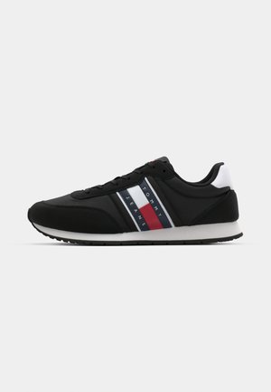 Chaussures de sport noires avec une tige en textile lisse, comportant des rayures horizontales blanches, rouges et bleues. Semelle en caoutchouc avec un profil texturé.