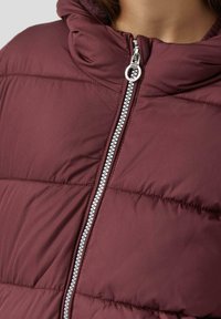 Burgundska jakna s punjenjem s visokim ovratnikom, s metalnim zatvaračem u srebrnoj boji i izvezenim dizajnom. Glatka tekstura, bez vidljivih uzoraka ili akcenta.