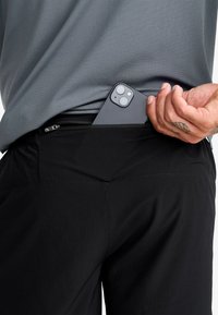 Black athletic shorts with a zippered pocket, featuring a textured gray shirt and a smartphone partially visible in the pocket.