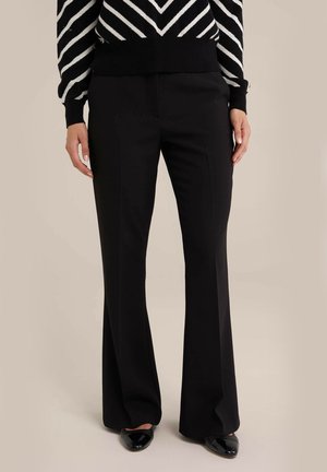 Pantalon noir à jambes droites porté avec des chaussures noires vernies à bout pointu et un pull à chevrons noir et blanc.