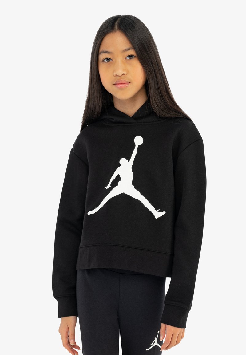 Črna skrajšana kapuca iz bombaža z dolgimi rokavi, z velikim belim Jumpman logotipom na sprednji strani. Obuta z črnimi hlačami.