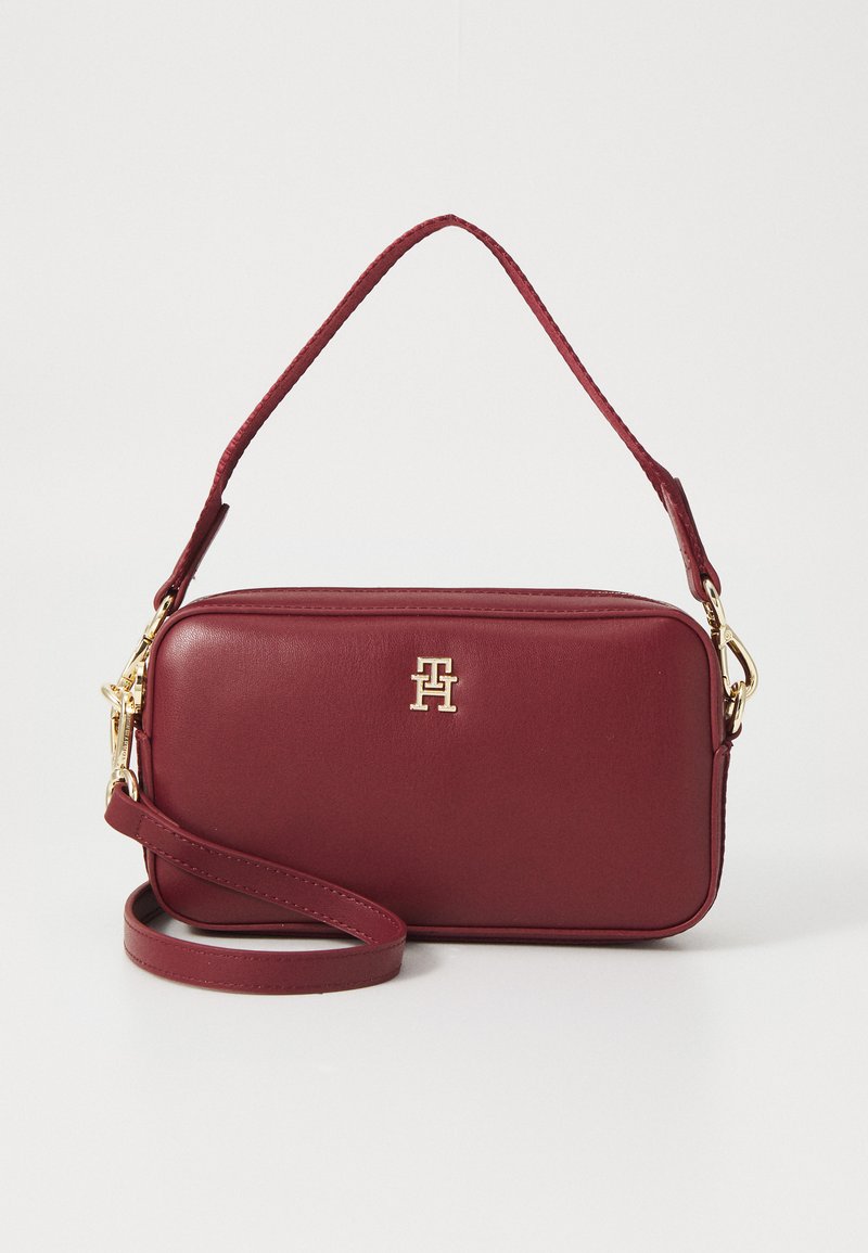 Burgunderfarbene Lederhandtasche mit einem goldenen Logo, rechteckiger Form, oberem Griff und abnehmbarem Schulterriemen. Glatte Textur, minimalistisches Design.
