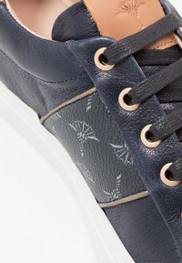 Baskets bleu marine en cuir texturé, avec un accent marron contrastant, des œillets dorés et une semelle blanche. Présentent un détail subtil à motif sur le côté.