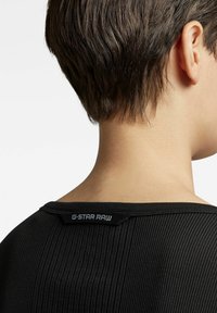 Schwarzes geripptes Shirt mit Rundhalsausschnitt und G-Star RAW Etikett auf der Rückseite. Nahaufnahme der Rückansicht, die Textur und Passform zeigt.