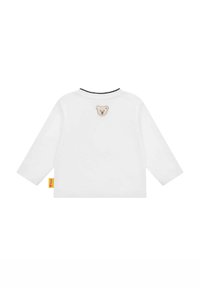 Camisa blanca de manga larga con cuello redondo, que presenta un pequeño aplique de oso en la parte posterior y una etiqueta de marca amarilla en el lado.