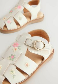 Sandale din piele albă cu broderie florală decorativă în roz, galben și verde. Vârf închis, curea cu cataramă, toc mic din lemn, spate deschis.