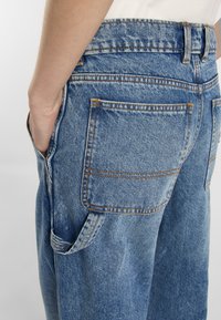 Nahaufnahme von blauen Denim-Jeans, die Details der Gesäßtaschen und eine Hand in der Tasche zeigen, und den lässigen Modestil hervorheben.