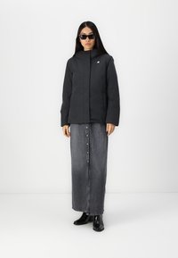 Giubbotto imbottito nero con cappuccio, abbinato a una lunga gonna di jeans con chiusura frontale a bottoni, e stivaletti neri alla caviglia. Design elegante.