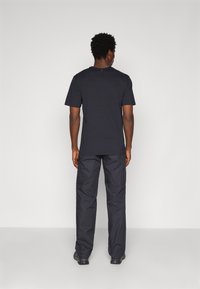 Black cotton t-shirt with short sleeves and a round neckline; paired with dark pants. Minimalist design, smooth texture, no visible graphics.