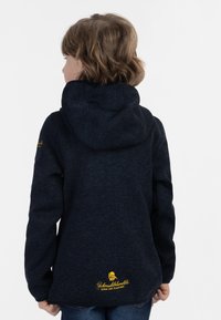 Felpa navy con finitura testurizzata, cappuccio regolabile e logo giallo ricamato sul retro. Maniche lunghe e vestibilità rilassata.