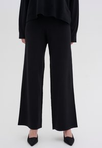 Black wide-leg pants made of soft fabric, featuring a smooth texture and a simple design. Paired with pointed black shoes.