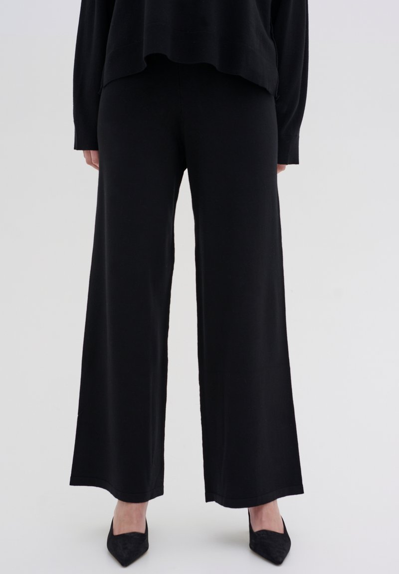 Black wide-leg pants made of soft fabric, featuring a smooth texture and a simple design. Paired with pointed black shoes.