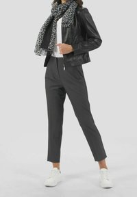 Černá kožená bunda, bílá košile, šedé kalhoty na míru a šedý šátek s leopardím vzorem, doplněné bílými teniskami.