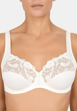 Femme portant un soutien-gorge écru avec des détails en dentelle florale sur le haut des bonnets et des bretelles larges de soutien.
