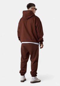Brauner Hoodie und passende Jogginghose, beide aus weichem Material gefertigt. Der Hoodie hat eine Kapuze mit Zugband; die Hose hat elastische Bündchen.