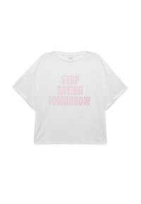 T-shirt bianco oversize con maniche corte, caratterizzato da un grande testo rosa che recita "SMETTILA DI DIRE DOMANI" nella parte frontale. Tessuto morbido al tatto.