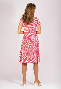 Dopasowana sukienka w różowo-białe paski z rozkloszowanym dołem, krótkimi rękawami i teksturowanym wzorem, w połączeniu z białymi butami na słupku.