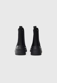 Schwarze Knöchelboots aus strukturiertem Stoff mit elastischen Seitenpaneelen. Sie haben eine robuste schwarze Gummisohle und ein Logo an der Ferse.