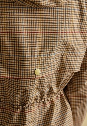 Houndstooth-patterned jacket in beige and brown with blue and red accents. Features a drawstring waist and a metallic snap button detail.