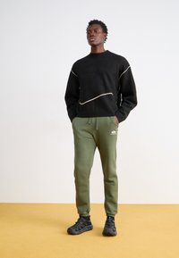 Sort sweater med hvide buede linjer, parret med grønne joggingbukser med elastiske manchetter og et logo. Komplet med sorte sko.