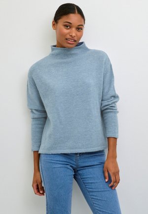 Light blue, soft-knit sweater with a high neckline and long sleeves, paired with blue jeans; relaxed fit and slightly cropped design.