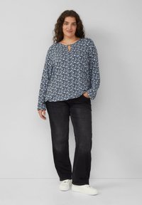 Blaue gemusterte Langarmbluse mit Schlüssel-Ausschnitt, kombiniert mit schwarzen geraden Jeans und weißen Sneakers. Glatte Stofftextur.