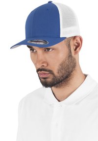 Blå basebollkeps med fast front och vit meshback. Har en kurvad sk�ärm och etikett på framsidan. Bärs av en modell i en vit polo.