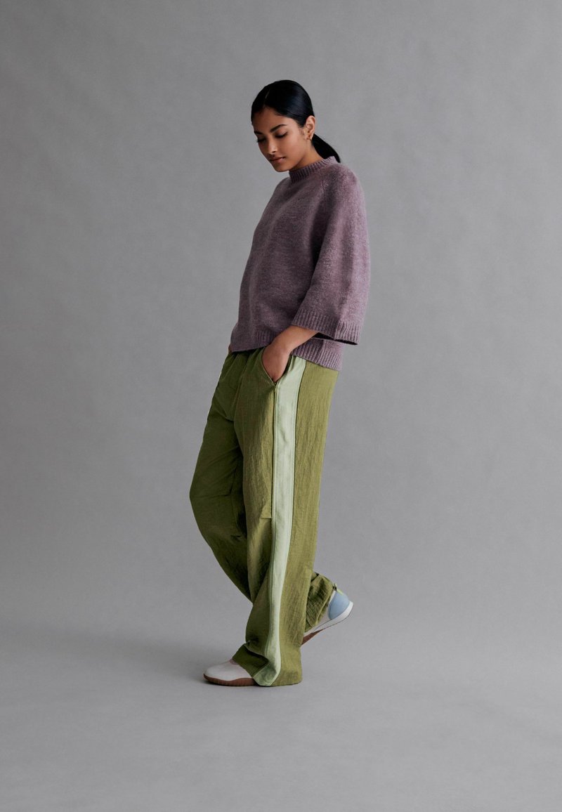 Lys lilla strikket sweater med trekvartærmer, parret med grønne vidde bukser med lysegrønne sidelommer. Afslappet fodtøj.