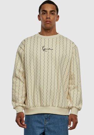 Sudadera color crema con un patrón de líneas onduladas negras, puños y dobladillo acanalados, y un pequeño logo negro en el pecho. Corte casual, material de felpa.