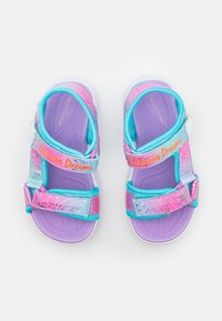 Multicolored sandals featuring a purple base, iridescent straps with pink and blue accents, and adjustable Velcro closures with "Unicorn Dreams" text.