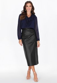 Tengerészkék blúz fodros nyakkivágással, fekete műbőr ceruzaszoknyával párosítva. A megjelenést átlátszó pántos magassarkú cipő teszi teljessé.