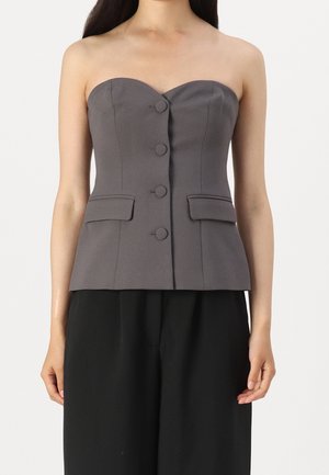 Kobieta w szarym topie bez ramiączek zapinanym na guziki z klapami kieszeniami, w połączeniu z czarnymi spodniami, widoczna od ramion do bioder.