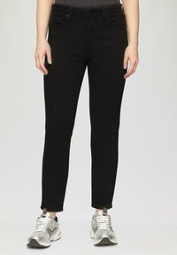 Czarne slim-fit dżinsy z średnim stanem, z kieszeniami i gładką fakturą materiału. Połączone z srebrnymi butami sportowymi.