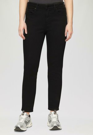 Jean slim noir à taille mi-haute, doté de poches et d'une texture de tissu lisse. Assorti à des chaussures de sport argentées.
