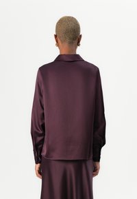 Satin shirt in deep purple, featuring a collar, long sleeves, and buttoned cuffs. Smooth texture with a relaxed fit at the back.