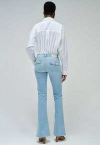 Jeans acampanados de color azul claro con un corte a media altura, que cuentan con dos bolsillos traseros y una cinturilla sencilla, combinados con una camisa blanca de botones.
