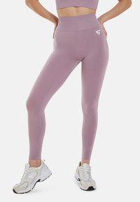 Lila visoka legging iz raztegnjenega blaga s gladko teksturo. Ima logotip na boku in kontrastne šive.