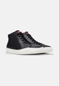 Zapatillas altas de cuero negro con parte superior texturizada, que cuentan con cordones negros, suela de goma blanca y marca roja en la lengüeta.