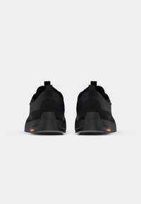 Black athletic shoes with a smooth texture, featuring a rounded shape, contrasting midsole, and Vibram branding in orange on the underside.