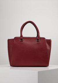 Czerwona skórzana torebka o wyraźnie zarysowanym kształcie, z dwoma uchwytami i srebrnymi akcesoriami. Gładka faktura bez widocznych wzorów.