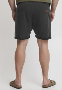 Sorte bomullsshorts med rullekant, elastisk midje og en baklomme. En brun lærlabel er synlig over høyre lomme.